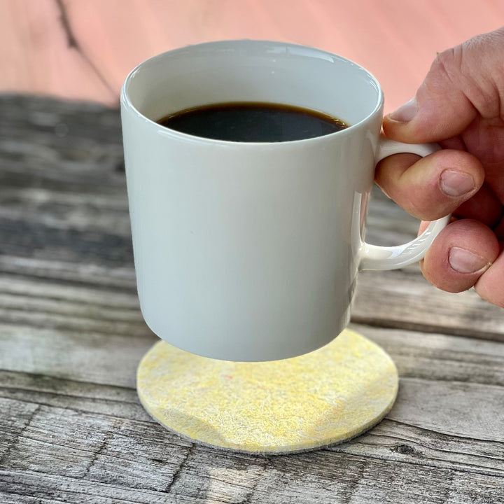 Lasinalunen VIIARI keltainen beige käytössä kuumalla kahvikupilla puupinnalla.
