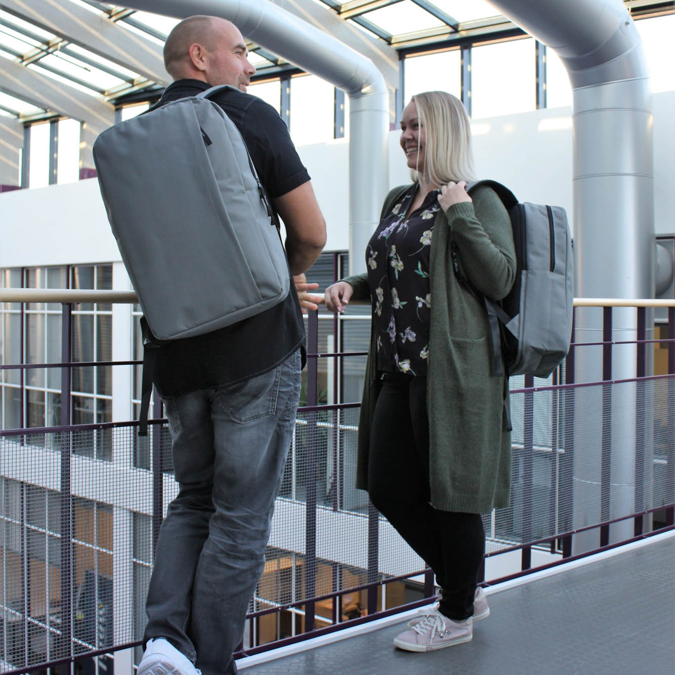 Harmaa selkäreppu, UITMUS 20 L, käytössä kahdella hengellä modernissa ympäristössä.